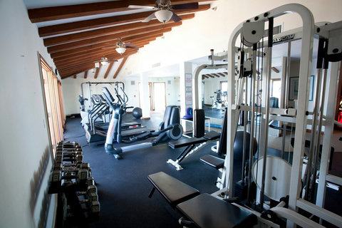 Spacious gym featuring treadmills, ellipticals, free weights, and strength machines under a stylish wooden beam ceiling.