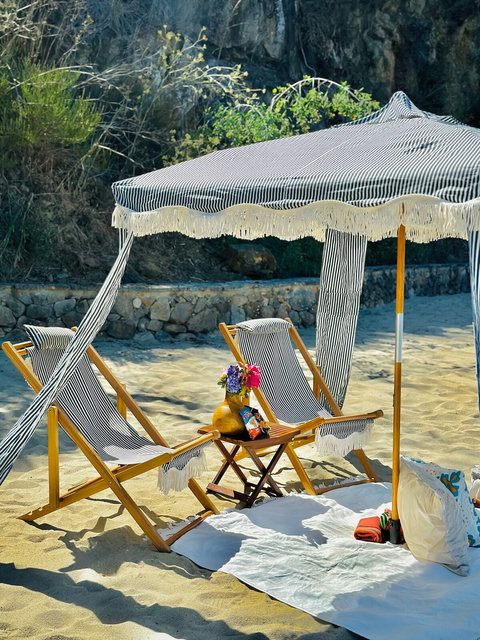 Nestled by rocky cliffs, this shaded cabana with cozy details invites you to a peaceful seaside escape.