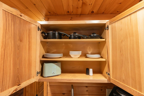 Open wooden cabinet with cookware, dishes, and a toaster for convenient meal preparation.