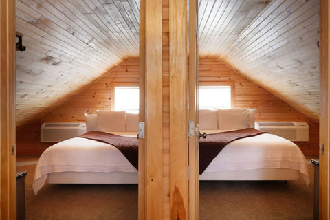 Cozy attic bedroom with wood-paneled walls and natural light from two windows.