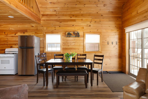 Rustic dining area with wooden walls and natural light from sliding glass doors.