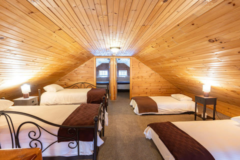 Spacious attic bedroom with four single beds and warm wood paneling for a cozy stay.