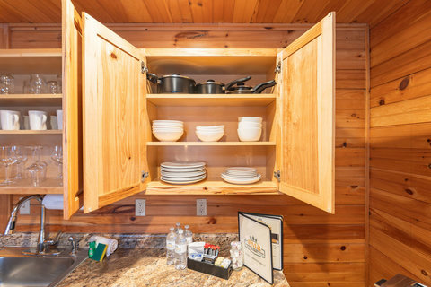 Open wooden cabinet displaying cookware and dishware in a rustic kitchen setting.