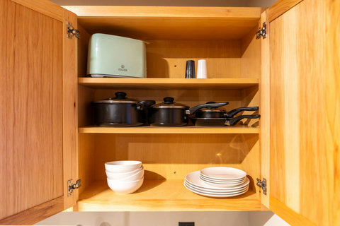 Wooden cabinet with cookware, plates, bowls, and a toaster for convenient meal preparation.