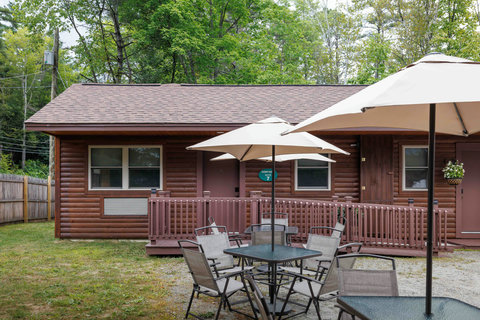 Outdoor seating area with umbrellas in front of a rustic cabin surrounded by trees