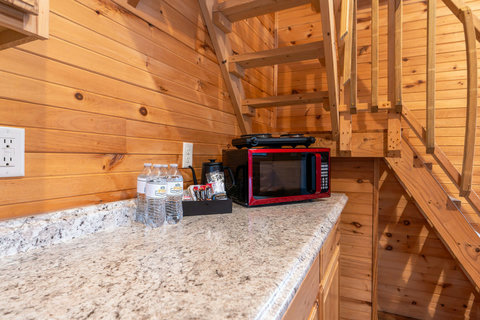 Compact kitchenette area with a microwave and coffee station under wooden stairs.