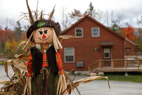 Rustic cabin with autumn decorations set against fall foliage.
