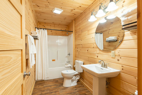 Rustic bathroom with wood-paneled walls and a full bathtub and shower.