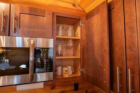 Open kitchen cabinet with glassware and mugs next to a stainless steel microwave