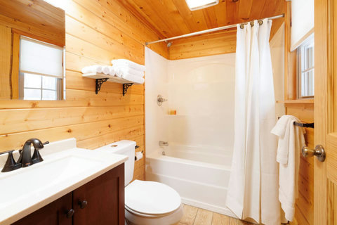 Rustic bathroom featuring a bathtub with shower and wood-paneled walls.