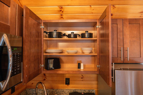 Open kitchen cabinet showing cookware, dishes, and a toaster in a wood-accented space.