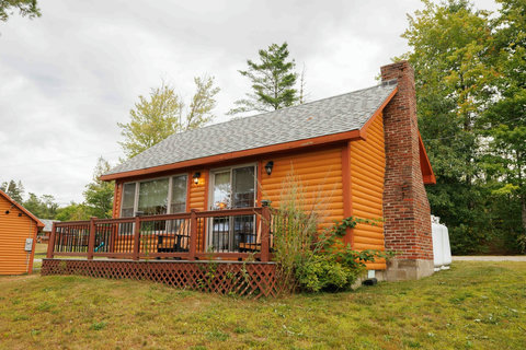Cozy cabin with a wooden deck and brick chimney surrounded by trees.