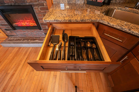 Organized kitchen drawer with utensils next to a cozy fireplace and granite countertop.