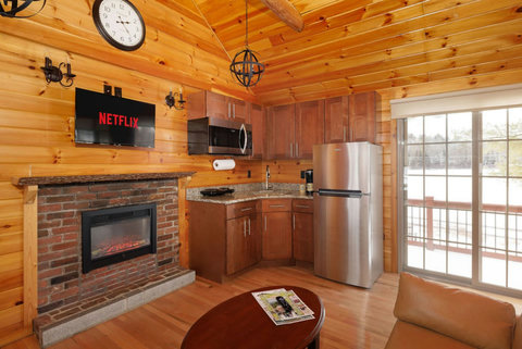 Cozy cabin kitchen with stainless steel appliances and a brick fireplace under a mounted TV.