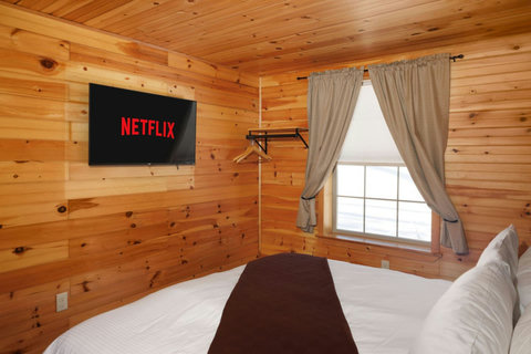 Cozy wood-paneled bedroom with a wall-mounted television and natural light from the window.