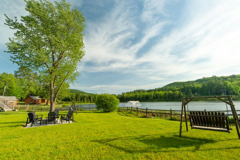 Lakeside yard with a fire pit seating area and wooden swing overlooking the water and forested hills.
