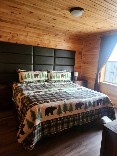 Cozy bedroom with wood-paneled walls and bear-themed bedding for a rustic cabin feel.