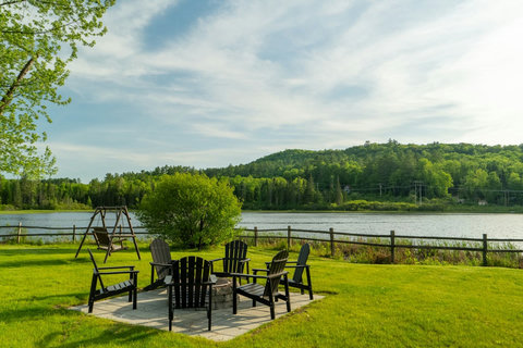 Outdoor seating area with fire pit overlooking a peaceful lake and forested hills.