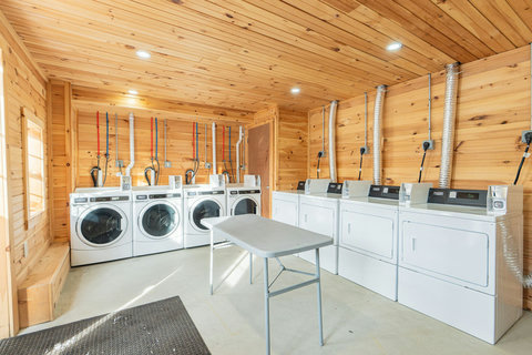 Laundry room with multiple washers and dryers in a wood-paneled space.