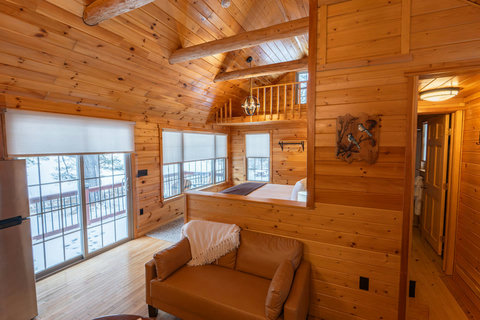 Cozy cabin interior with wood paneling and large windows overlooking a snowy landscape.