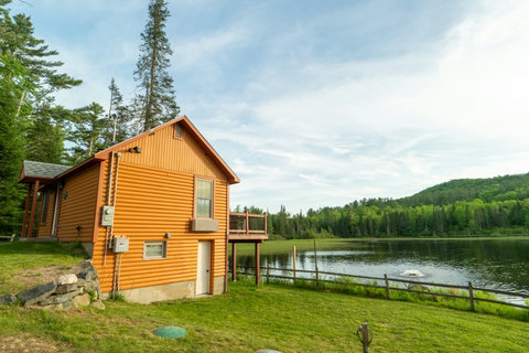Rustic cabin with a deck overlooking a peaceful lake and forested hills.
