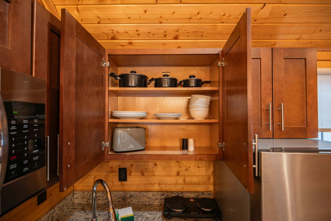 Open kitchen cabinet showing cookware, dishes, and a toaster in a rustic wood interior.