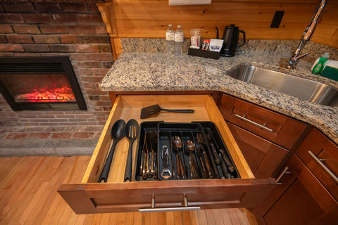 Open kitchen drawer with organized utensils next to a granite countertop and fireplace.