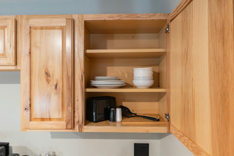 Open wooden kitchen cabinet with neatly arranged dishes and utensils