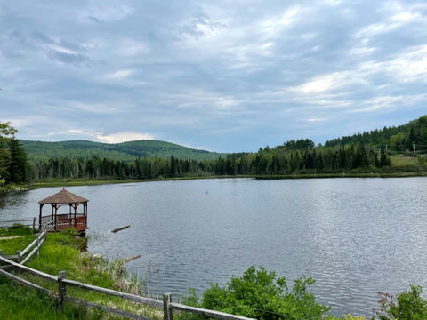 Tranquil lake view with a wooden gazebo and surrounding forested hills.
