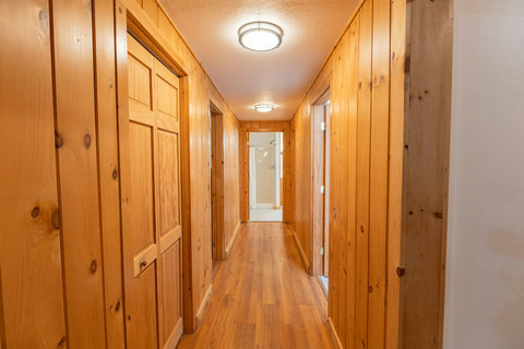 hallway with wood-paneled walls and hardwood floors leading to a bathroom