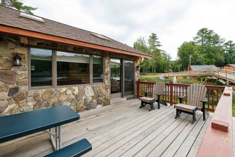 Rustic stone cabin deck with seating overlooking a peaceful pond and wooden bridge.