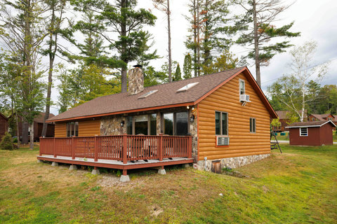 Rustic cabin with a spacious wooden deck surrounded by trees.