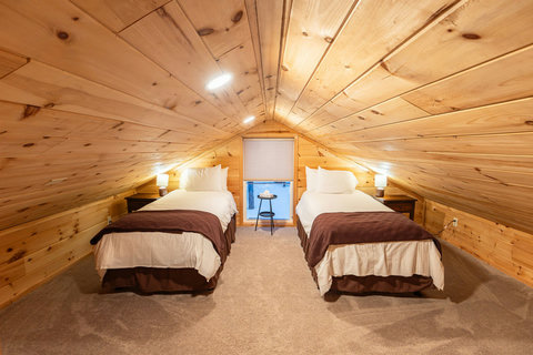 Cozy attic bedroom with twin beds and warm wood paneling for a comfortable stay.