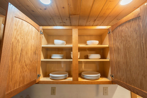 Open wooden kitchen cabinet with neatly organized white dishes under warm lighting