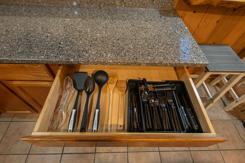Organized kitchen drawer with essential cooking utensils and cutlery under a granite countertop.