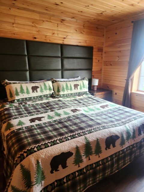 Rustic bedroom featuring a king-size bed with bear and pine tree patterned bedding and wood-paneled walls.