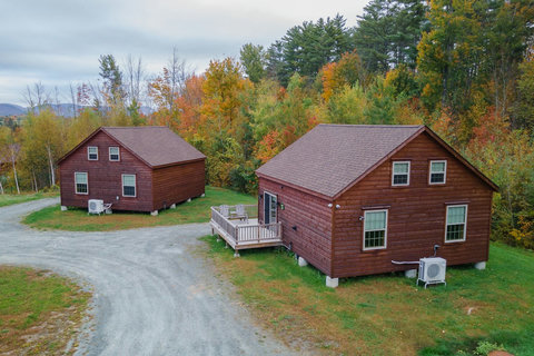Two rustic cabins surrounded by colorful autumn trees with a gravel driveway.
