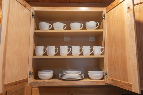Open wooden cabinet with neatly arranged white mugs, plates, and bowls