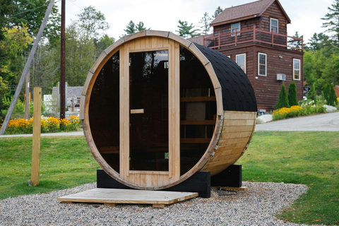 Outdoor wooden barrel sauna with glass door set in a natural garden setting