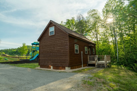 Rustic cabin with a wooden deck surrounded by trees and a nearby playground for family-friendly outdoor fun.