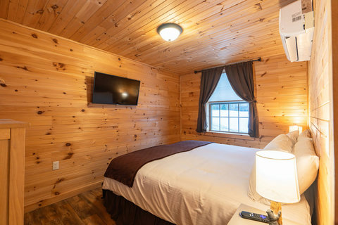 Cozy bedroom with wood-paneled walls and a mounted flat-screen television.