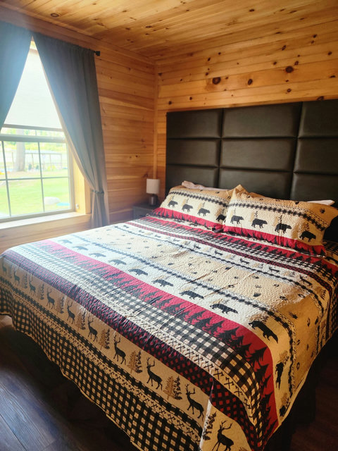 Cozy bedroom with rustic wood walls and wildlife-themed bedding next to a large window.