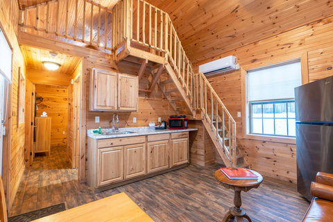 Cozy cabin kitchen with wooden interiors and a loft staircase.