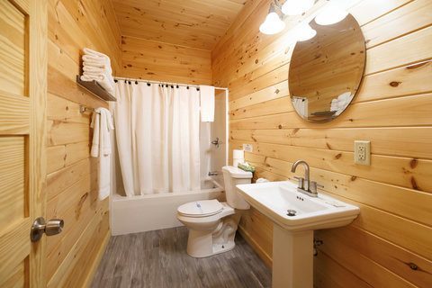 Rustic bathroom with wood-paneled walls, a bathtub with shower, and a pedestal sink.