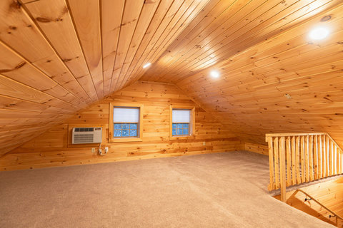 Cozy loft space with wood-paneled walls and ceiling, featuring two windows and carpeted flooring.