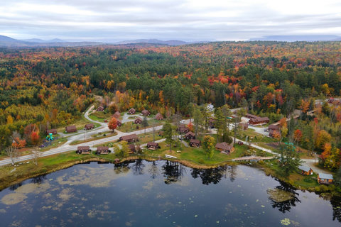 A lakeside cabin community surrounded by colorful autumn forest and rolling hills.