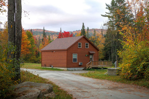 Cozy cabin surrounded by vibrant autumn foliage and forested hills.