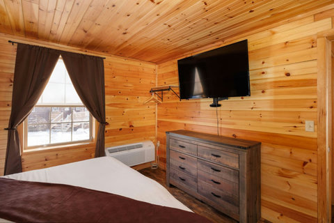 Cozy bedroom with wood-paneled walls, a mounted flat-screen tv, and natural light from the window.