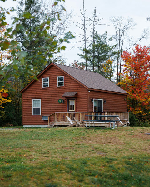 Rustic cabin with a spacious deck and picnic area surrounded by autumn trees
