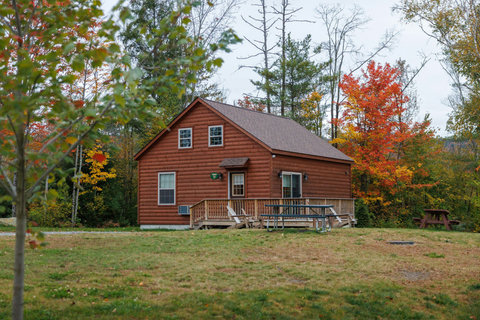 Cozy rustic cabin surrounded by colorful autumn trees with outdoor seating on the deck.